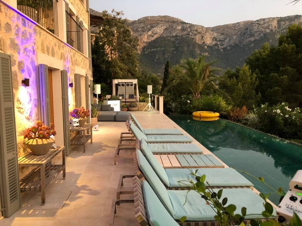 Poolside view of a villa with lounge chairs, plants, and a scenic mountain backdrop at sunset.
