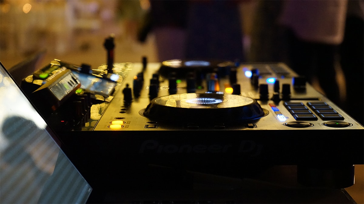 Close-up of a DJ mixer and turntables with colorful lights in a dimly lit setting.
